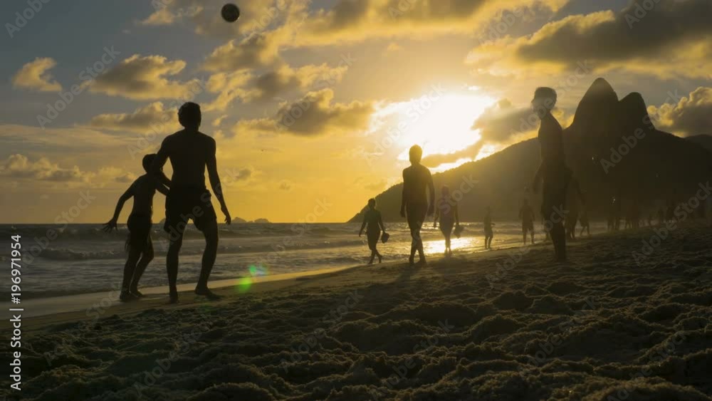 Playing beach football at sunset on Ipanema Beach in Rio de Janeiro. People silhouettes with iconic mountains as background. Slow motion Playing beach football at sunset on Ipanema Beach in Rio de Janeiro. People silhouettes with iconic mountains as background. Slow motion