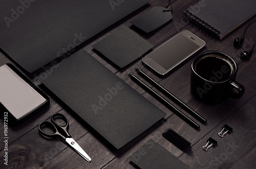 Blank black corporate stationery with phone on dark stylish wood background, inclined, closeup. Branding mock up for branding, graphic designers presentations and business portfolios.
