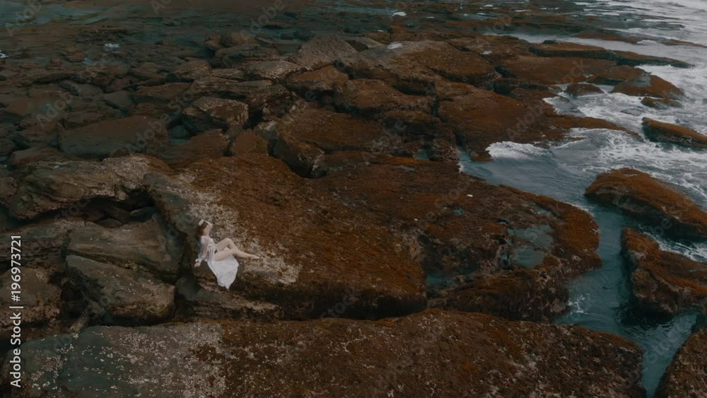 Beautiful slender young female in a long sexy dress poses on the rocks on the ocean beach on Bali on the sunset, shooting video 4K from the aircraft from above, wonderful view, amazing model Beautiful slender young female in a long sexy dress poses on the rocks on the ocean beach on Bali on the sunset, shooting video 4K from the aircraft from above, wonderful view, amazing model