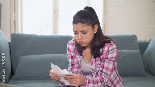 lateral panning of young attractive worried hispanic woman checking bills bank papers expenses and monthly payments stressed sititing at apartment couch in domestic stress finance problem 