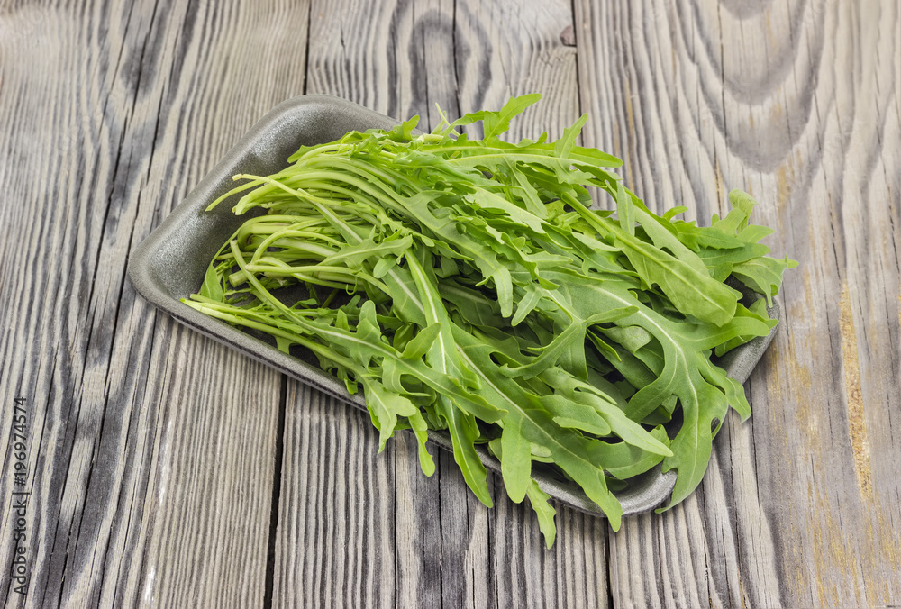 Arugula in foam food container on an old wooden surface Arugula in foam food container on an old wooden surface