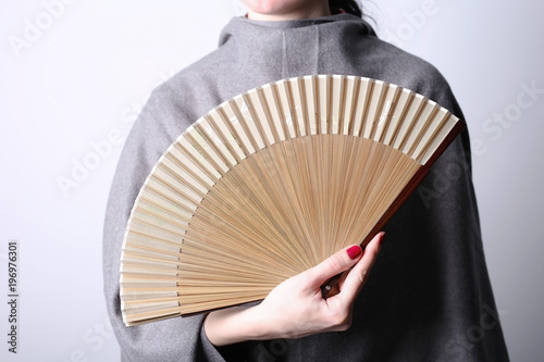 A womand in grey holds in her hand a fan to hide her face