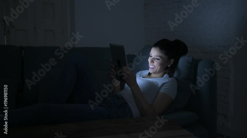 lateral pan shot of young beautiful happy and relaxed latin woman lying on home couch late night using digital device laptop tablet pad watching internet movie 