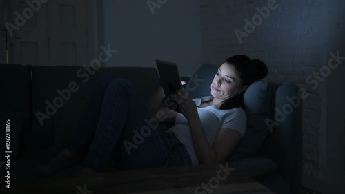 lateral pan shot of young beautiful happy and relaxed latin woman lying on home couch late night using digital device laptop tablet pad watching internet movie 