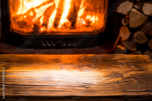 Old wooden table and fireplace with warm fire at the background.