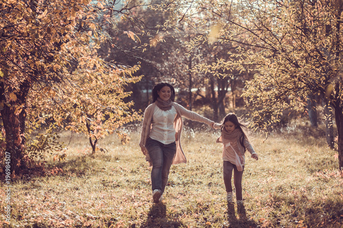 Happy woman and smiling kid spend time together in golden autumn garden.