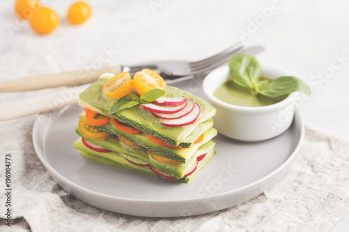 Raw vegan zucchini lasagna with vegetables and pesto sauce, light background. Vegetarian raw diet concept.