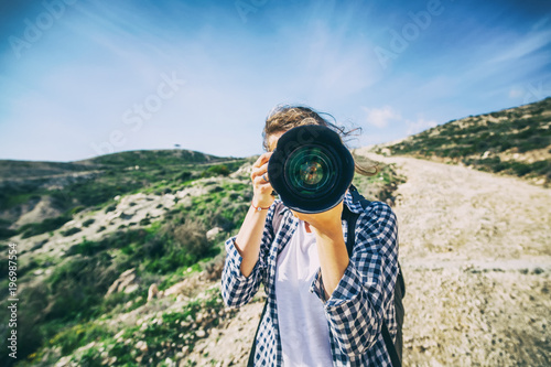 Girl traveler with a camera in hand, against a beautiful summer landscape, a lens on a viewer, travel, a blogger, summer vacation, freedom, hiking concept