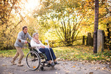 Senior man and woman in wheelchair in autumn nature.