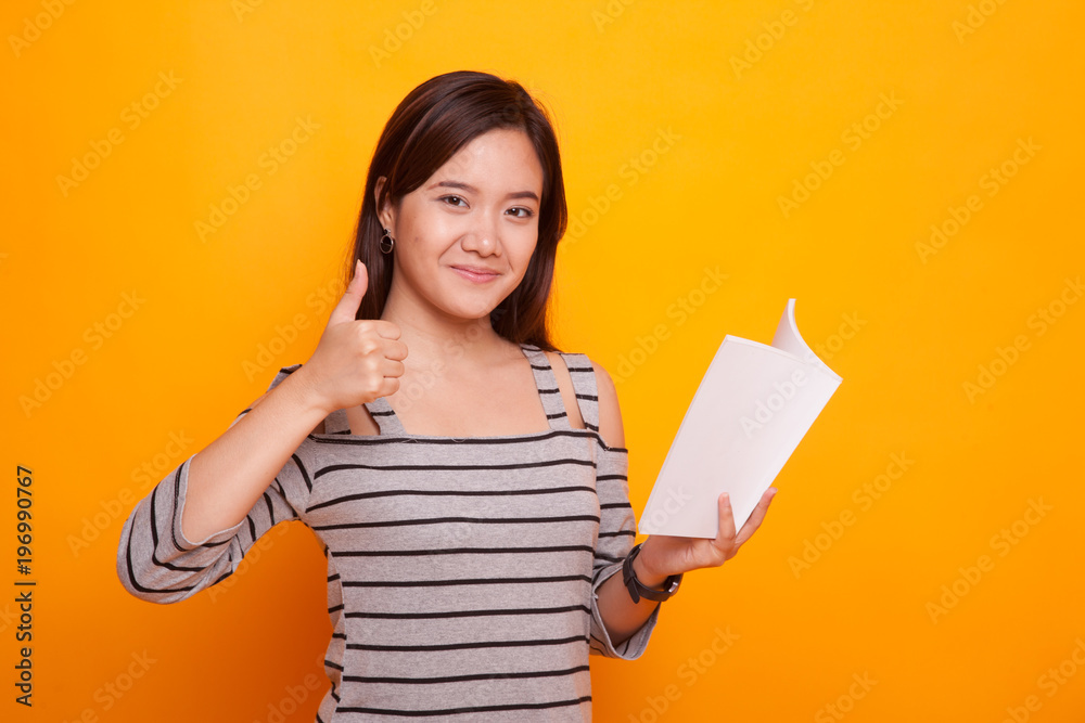 Young Asian woman thumbs up with a book. Young Asian woman thumbs up with a book.