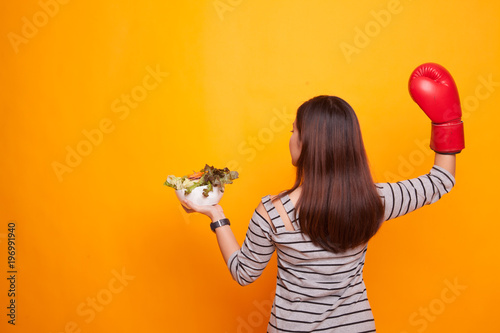 Young Asian woman with boxing glove and salad.