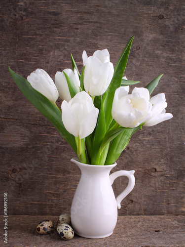 Fototapeta Naklejka Na Ścianę i Meble -  Bouquet of white tulips in a white jug on an old wooden background.