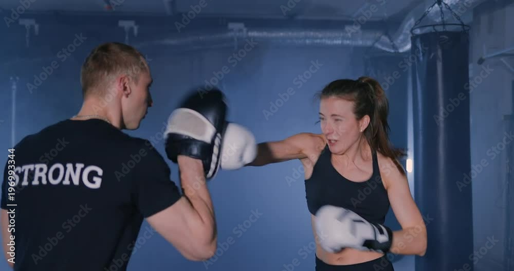 Young woman with trainer at boxing and self defense lesson in a smoky gym Young woman with trainer at boxing and self defense lesson in a smoky gym