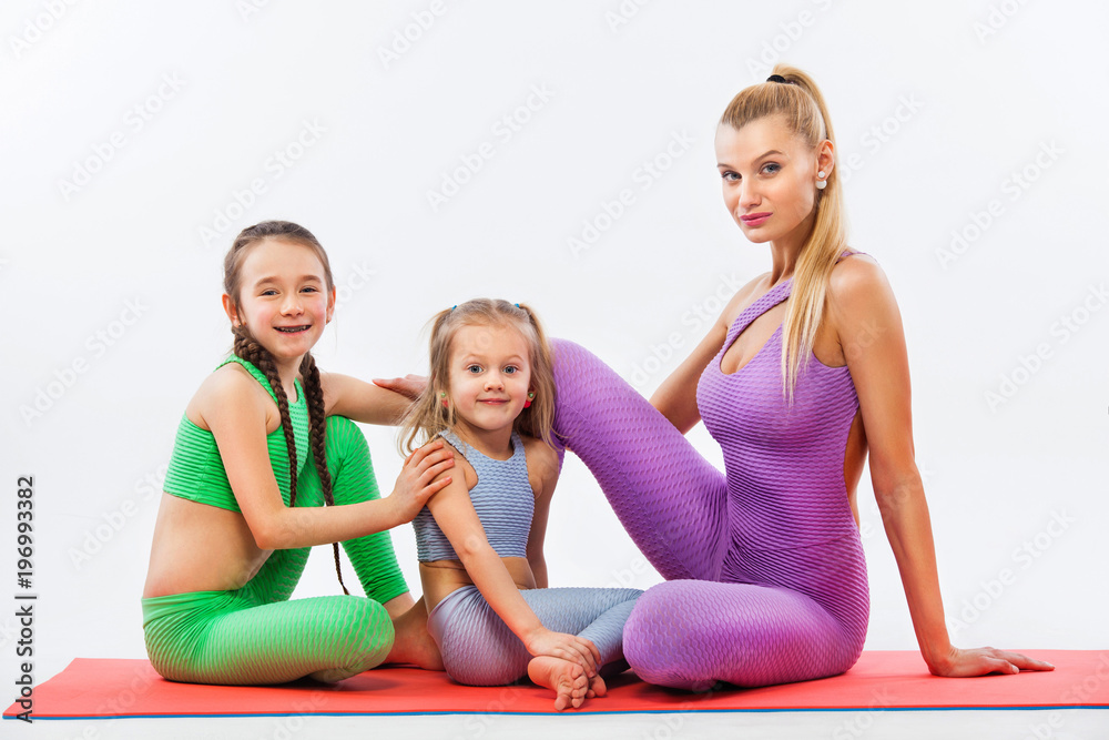 Hatha yoga. Kids fitness . Young mother Instructor and daughters exercise gymnastic together. Isolated on white background. Family look. Hatha yoga. Kids fitness . Young mother Instructor and daughters exercise gymnastic together. Isolated on white background. Family look.