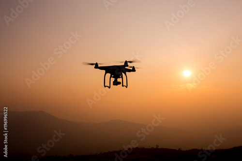 Drone silhouette flying in sunset landscape.  © sanee