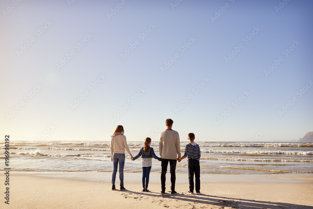 Rear View Of Family On Winter Beach Holding Hands Looking At Sea