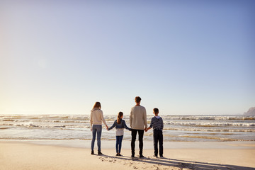 Rear View Of Family On Winter Beach Holding Hands Looking At Sea