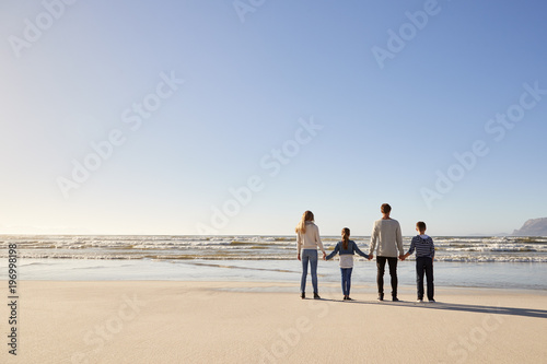 Rear View Of Family On Winter Beach Holding Hands Looking At Sea © Monkey Business