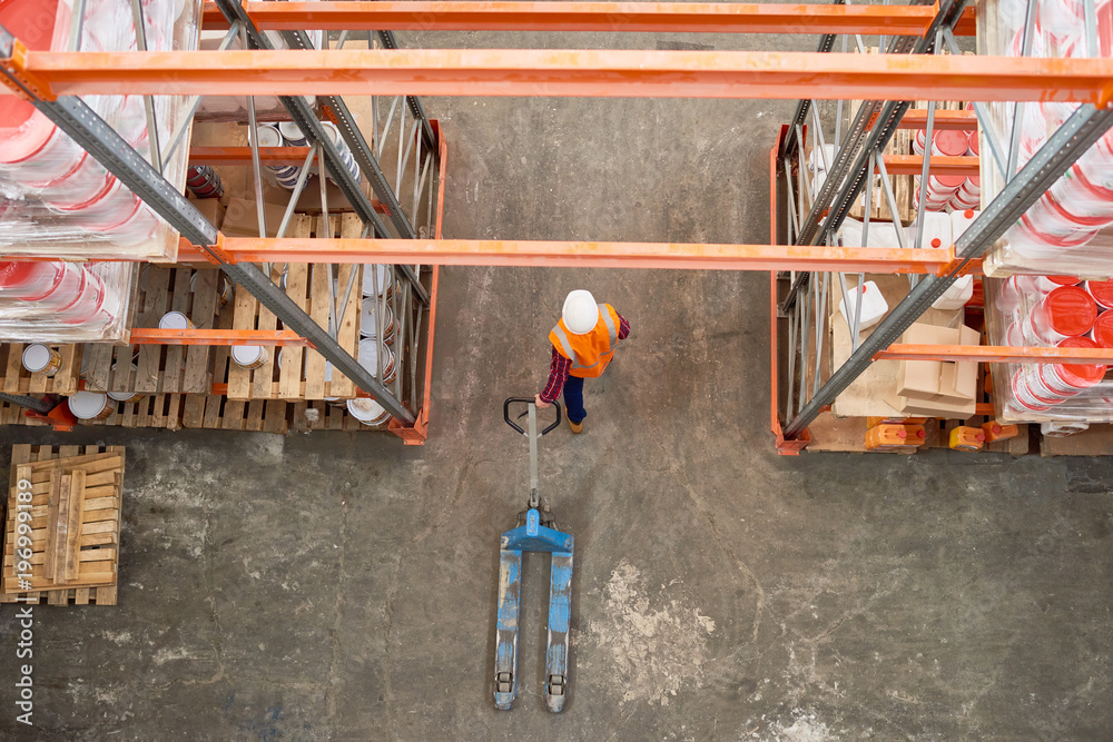 Top view background image of tall shelf rows in modern warehouse with worker wearing hardhat pulling empty cart in aisle, copy space