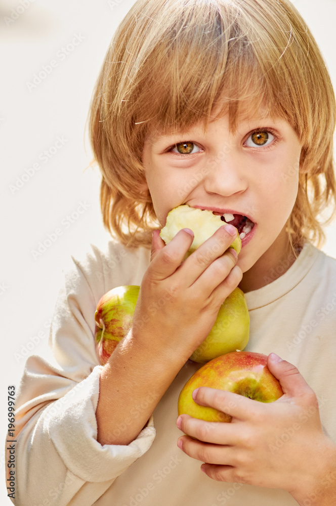 Portrait of cute little blonde boy with milk teeth eating apple