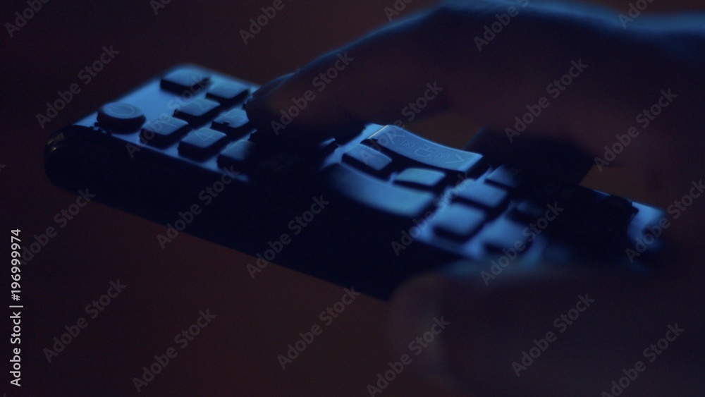 Fototapeta premium closeup of tv controller and man's hand pushing buttons in screenlight