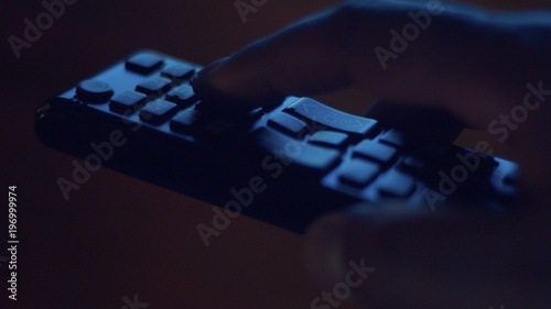 closeup of tv controller and man's hand pushing buttons in screenlight