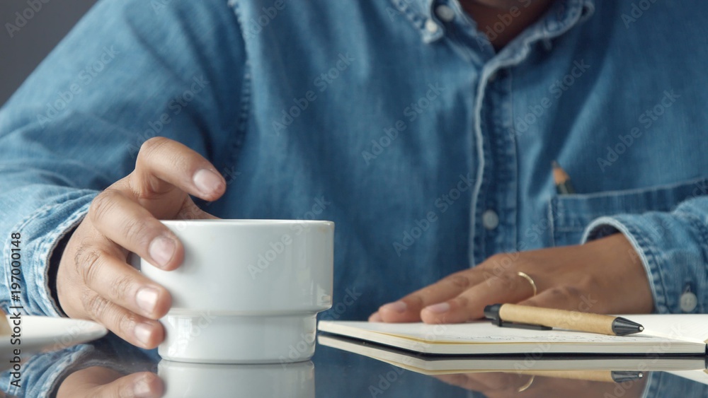closeup man's hands making notes.and picking cup of coffee closeup man's hands making notes.and picking cup of coffee