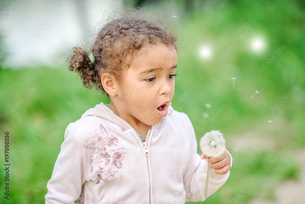 Toddler girl with curly hair playing with yellow dandelions in a blooming spring and summer garden Toddler girl with curly hair playing with yellow dandelions in a blooming spring and summer garden