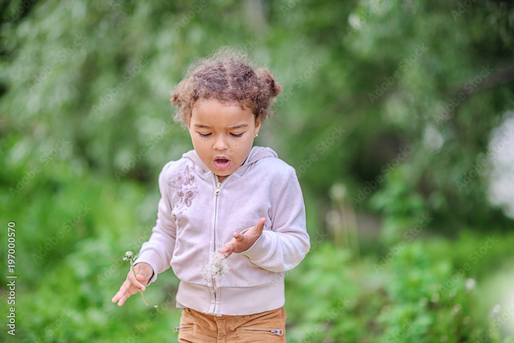 Toddler girl with curly hair playing with yellow dandelions in a blooming spring and summer garden Toddler girl with curly hair playing with yellow dandelions in a blooming spring and summer garden