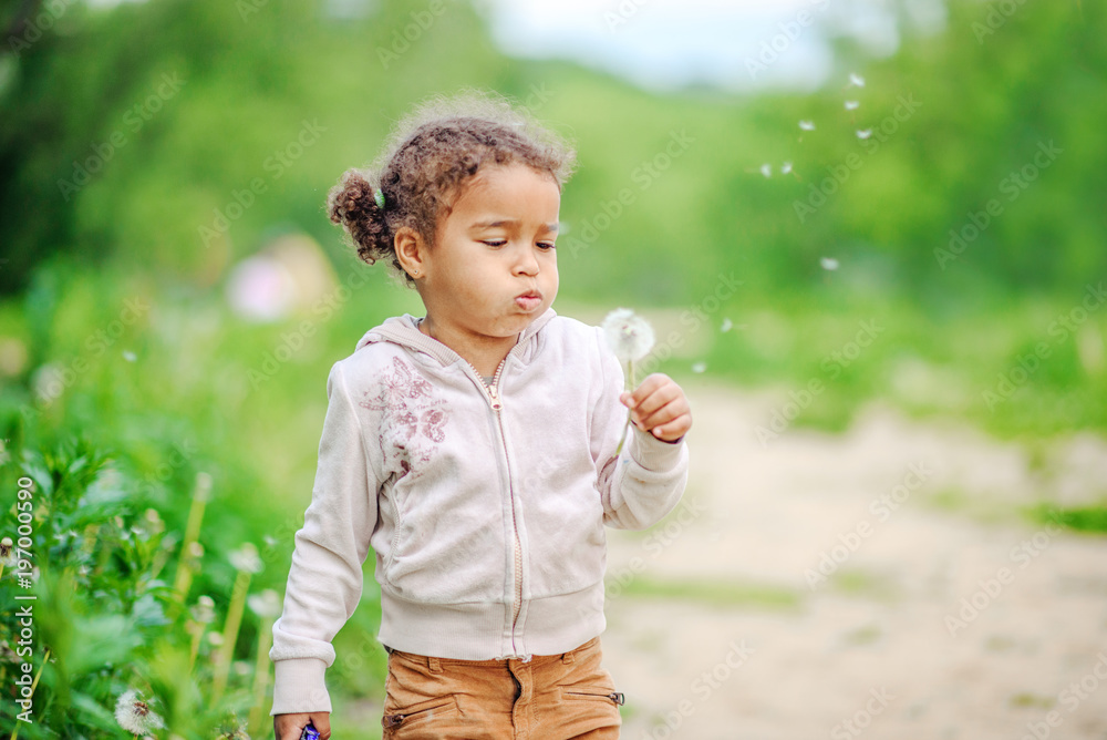 Toddler girl with curly hair playing with yellow dandelions in a blooming spring and summer garden Toddler girl with curly hair playing with yellow dandelions in a blooming spring and summer garden