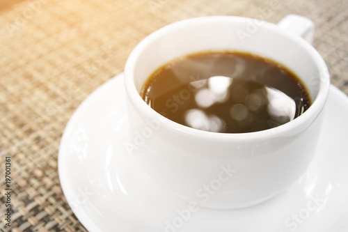 aroma hot black coffee with bokeh and smoke in white cup on the table for refreshing morning drink with space and sunlight, cup focus for bokeh on the water