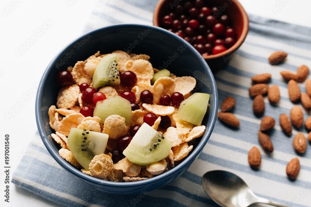 Delicious crispy cornflakes with kiwi pieces and cranberries in bowl, almonds on dish cloth, closeup, healthy breakfast Delicious crispy cornflakes with kiwi pieces and cranberries in bowl, almonds on dish cloth, closeup, healthy breakfast