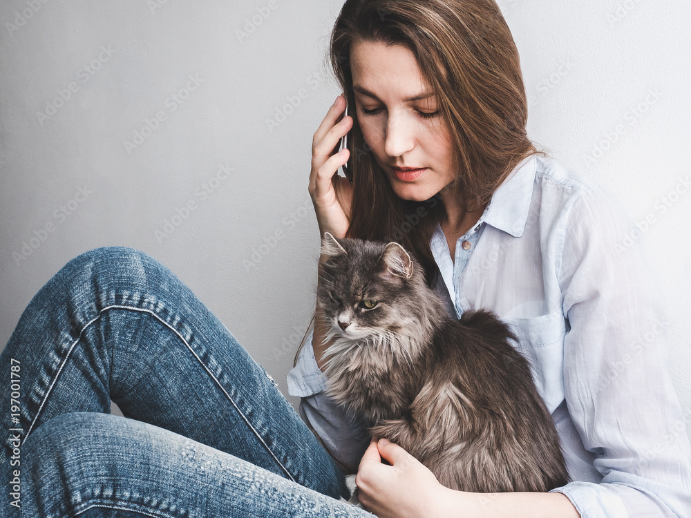 Stylish, young woman with mobile phone gently holding a kitten on a white background. People, care, pets, technologies Stylish, young woman with mobile phone gently holding a kitten on a white background. People, care, pets, technologies