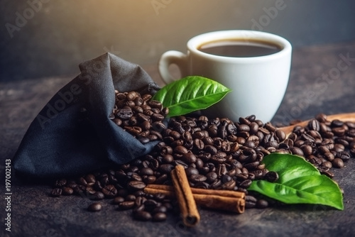 White black espresso Cup with pile of coffee beans and green leaves in bag on dark background
