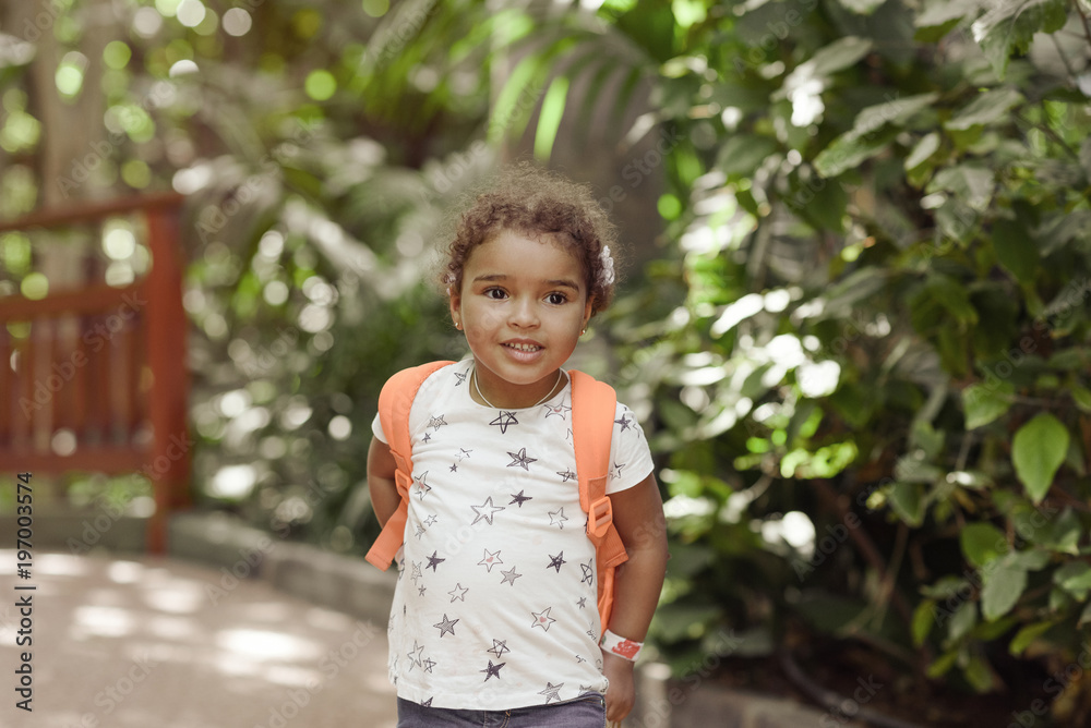 Portrait of little mixed-race girl smiling happily, background of green bamboo trees.
