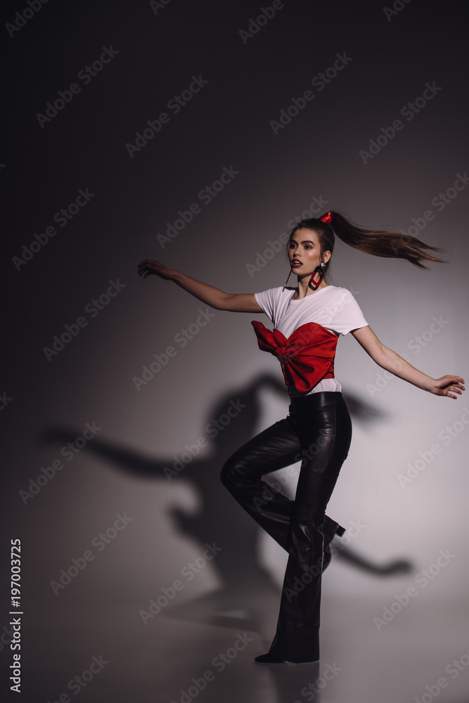 fashionable young woman in stylish clothing dancing alone on black background
