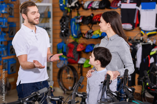 smiling young worker showing bicycles to mother and son in bike shop