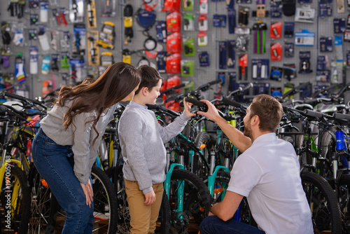 manager helping to choose bicycle to happy mother and son in bike shop