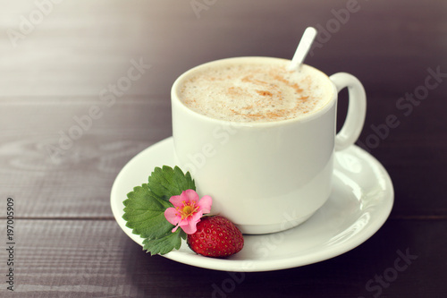 strawberry coffee pause with mood/ red ripe berry with flower and leaf next to a cup of foamy cappuccino sprinkled with cinnamon