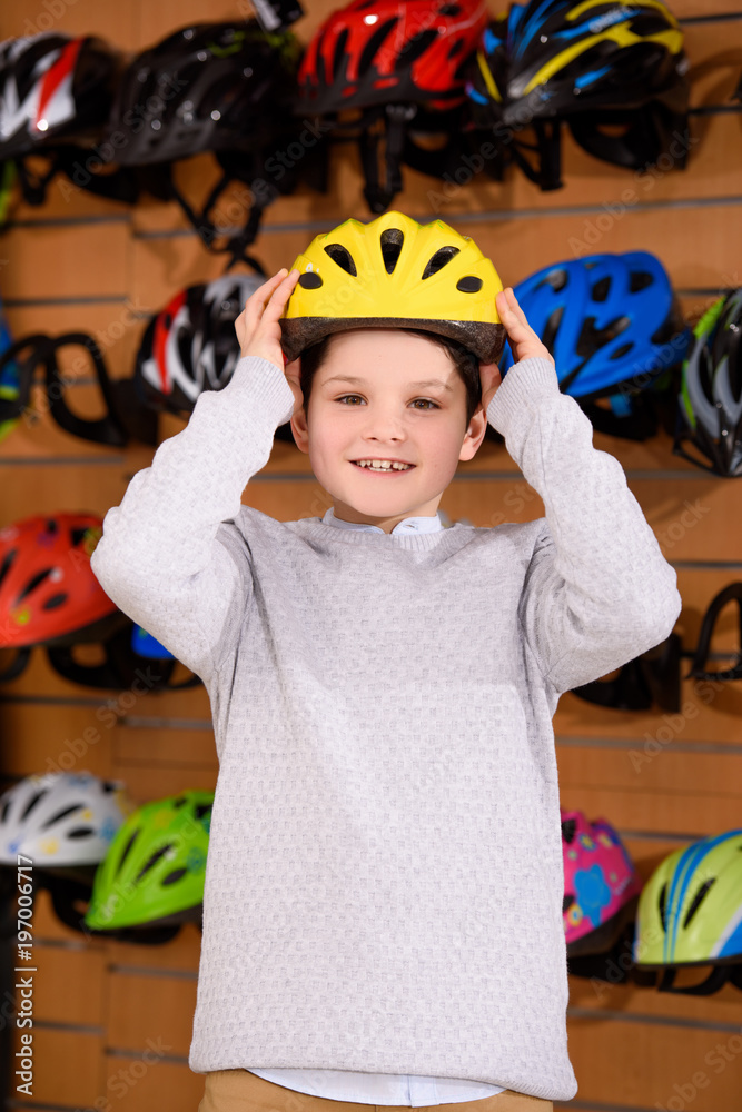 cute little boy putting on bicycle helmet and smiling at camera in bike shop cute little boy putting on bicycle helmet and smiling at camera in bike shop