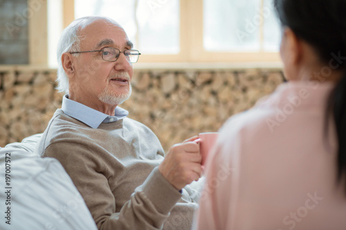 Tea time. Attractive pleasant senior man talking while posing on blurred background and enjoying life