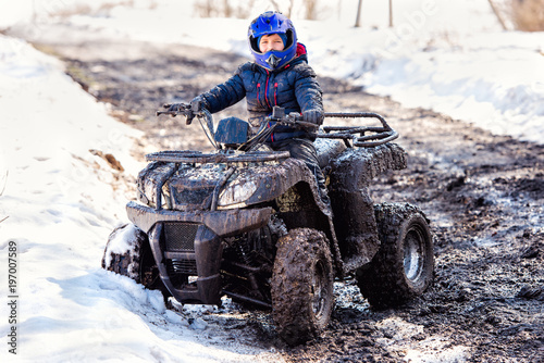 The boy is riding an ATV off-road.