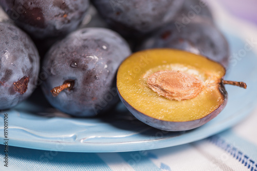 Fresh ripe blue plums on plate, wooden table with napkin