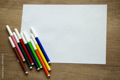 white sheet of paper, colored felt-tip pens on a wooden background 