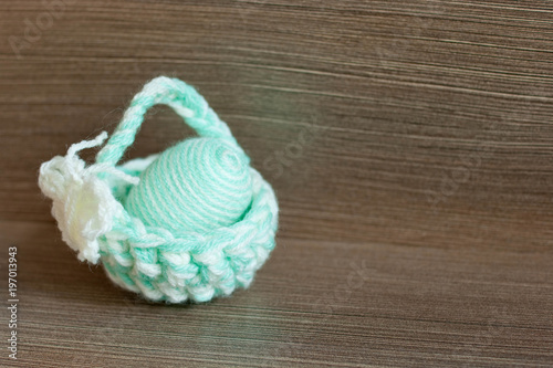 Easter decoration, crochet mini basket, striped colorful egg wrapped in soft yarn thread, pastel colors, butterfly, wooden texture background. Homemade decor. Shallow depth of focus. Easter holidays.