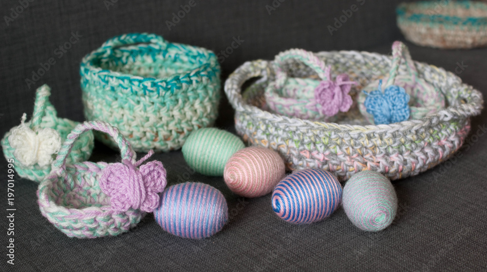 Easter decoration, crochet basket, striped colorful egg wrapped in soft yarn thread, pastel colors, butterfly, dark grey texture background. Homemade decor. Shallow depth of focus. Easter holidays.