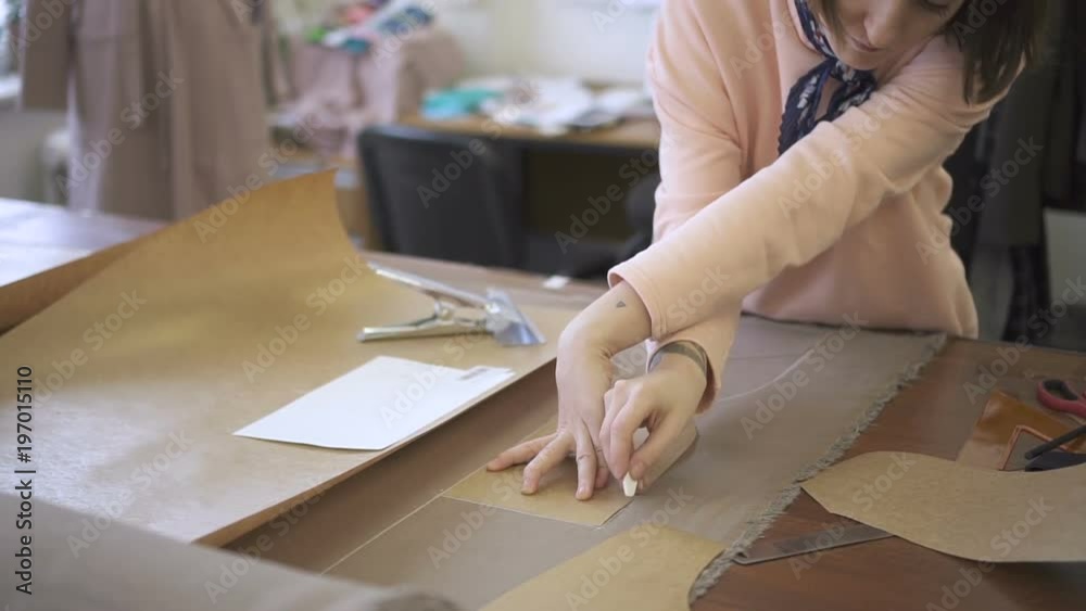 On table tailor circled with a chalk a pattern on material for sewing. Close-up of a woman doing a white drawing on the patterns for making individual clothes.