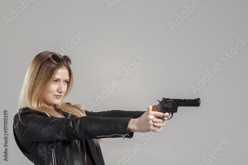 A girl in a leather jacket holds a revolver in her hands, danger, self-defense. The image of a confident and strong woman