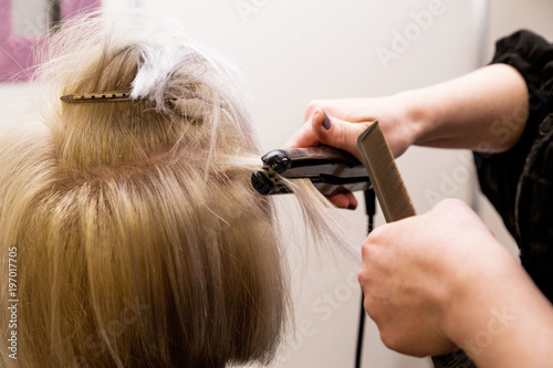 the hairdresser straightens hair with an iron