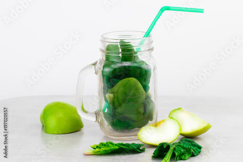 Green smoothie in glass jar with fresh organic green vegetables and fruits on grey background. Spring diet, healthy raw vegetarian, vegan concept, detox breakfast, alkaline clean eating.